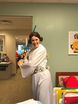 a woman dressed up an leia skywalker holding a plastic lightsaber